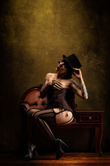 Portrait of a young sexy woman in Victorian lingerie, wearing a top hat and a pair of glasses.