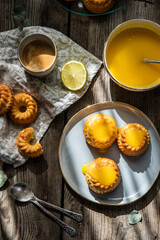 Shaped mini bundt cakes filled  with lemon curd and cup of coffee on old wooden table.