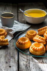 Shaped mini bundt cakes with lemon curd and cup of coffee on old wooden table.