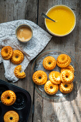 Shaped mini bundt cakes with lemon curd and cup of coffee on old wooden table.