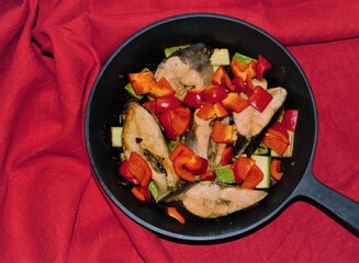 Cast-iron pan with a bright dish of vegetables and seafood on a red linen tablecloth