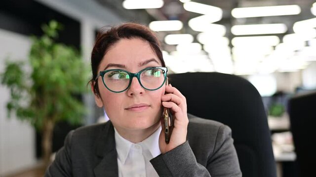 A woman sits in an office at her desk and gossips on the phone. Corporate ethics. Female employee in a suit tells secrets on a smartphone at work.