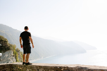 Muscular guy  stands on the shore, looking at the Italian landscape.
