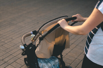 Side view of mother strolling her baby in carriage outdoors. Sunny day. Closeup shot.
