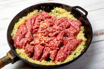 minced meat and onions in a pan on a light wooden background. Cooking toppings.