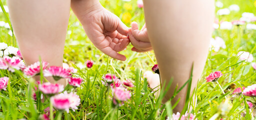 Obraz na płótnie Canvas Small baby bare legs,feet of little girl in grass with flowers of daisies.Summer concept.Kids walk in garden,field,meadow.Quarantine end,coronavirus covid-19.Staycation in vacation home,country house