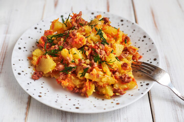 Baked potatoes with minced meat, onions and carrots baked on a plate on a light wooden background.