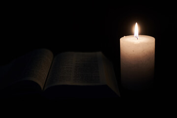 Burning candle and opened bible, book. The concept of faith in God, Christianity, religion.