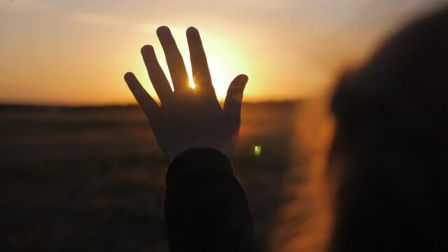 Girl looks at the sun through her hand at sunset.