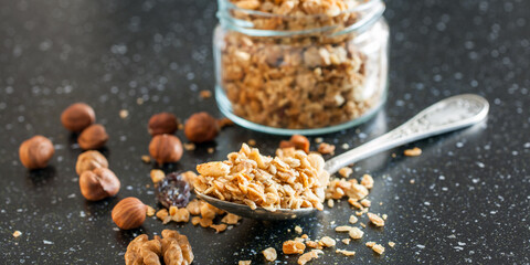 muesli or homemade granola with nuts in a spoon from a jar on a table, selective focus
