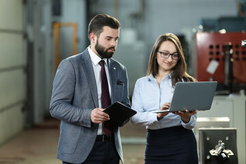 Portrait of a solid businessman with his secretary holding laptop and tablet, talking about factory financial report. Industrial workers.