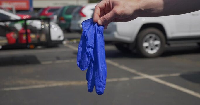 A man holds up then drops a pair of used surgical rubber gloves in a store's parking lot. Littering concept. Shot at 48 slow motion.  	