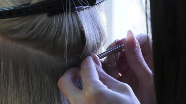 Artificial hair for extension in a beauty salon close up. Professional process of hair extension for a blonde woman with the help of artificial, in a beauty salon close up. 
