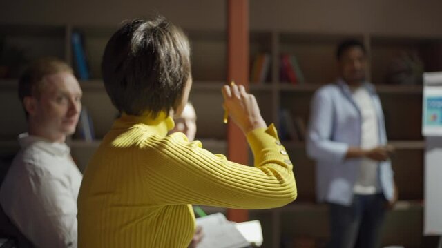 Tracking tilt up shot of people listening to speaker and taking notes at business seminar. Woman raising hand and asking business coach a question