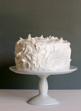 Frosted white cake on stand with gray background