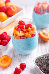 Layered chia seeds pudding with apricot, raspberry in glasses on white wooden background. Mousse with chia seeds, berries and fruits for healthy breakfast, top view