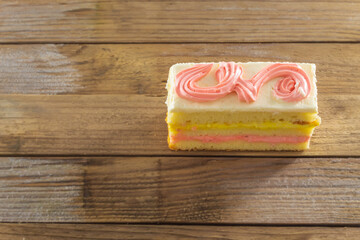 On a wooden background a rectangular fresh cake with cream