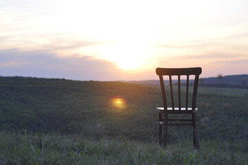 An old antique chair stands on the grass. At sunset. Summer. The concept of meditation and loneliness.