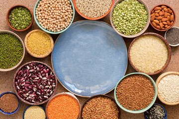 Empty blue plate and frame of various legumes, grains, seeds in bowls. Top view, flat lay, space for your text.