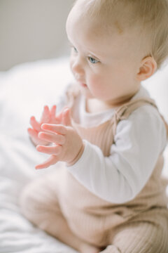 Baby girl clapping hands on bed in soft light