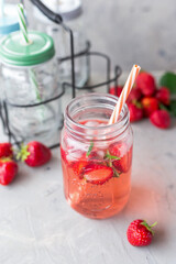 Strawberry lemonade with rosemary and ice in mason jar on a gray concrete table. Seasonal food concept. Summer harvest time