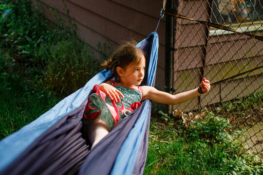 A small girl in a bright colored tutu plays in a hammock in sunshine