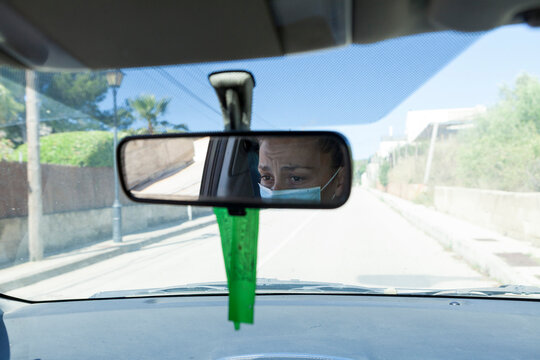 Image of a woman reflected in the rear view mirror of the car driving The woman wears a surgical mask on her face to protect herself from covid-19 during the coronavirus pandemic