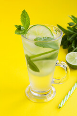 Infused water or cold lemonade with lime, ice and  mint  in the glass  on the yellow background. Location vertical. Copy space.