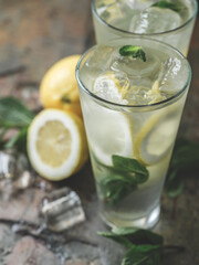 Fresh lemonade cocktail with ice, mint and lemon by barista cooked on table bar background with ingredients.