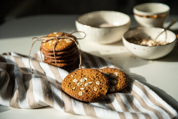 Homemade oatmeal cookies and bowls with ingredients on white kitchen table.