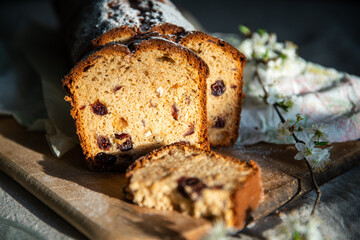 Sliced homemade pound cake with dried berries, vintage glass plates and blooming cherry twigs on linen tablecloth.