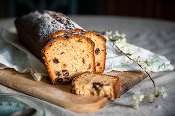 Sliced homemade pound cake with dried berries, vintage glass plates and blooming cherry twigs on linen tablecloth.