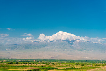 Fototapeta premium Ararat peak behind the clouds on a background of green field, beautiful landscape of Armenia