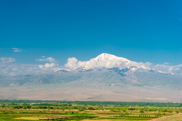Ararat peak behind the clouds on a background of green field, beautiful landscape of Armenia