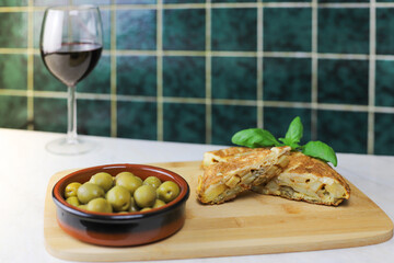 Delicious Spanish potato omelette topped with olives and cheese. Typical Spanish food. Glass of wine in the background.