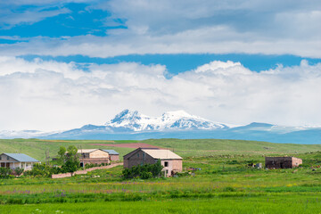 Fototapeta na wymiar Private houses in the field against the backdrop of beautiful snow-capped mountains in Armenia