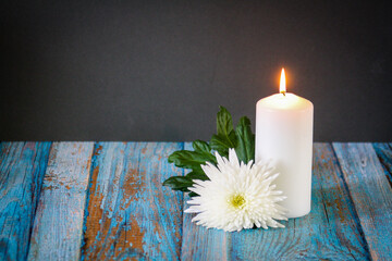 Close up of pillar burning candle and white flower on a blue surface with dark black background....