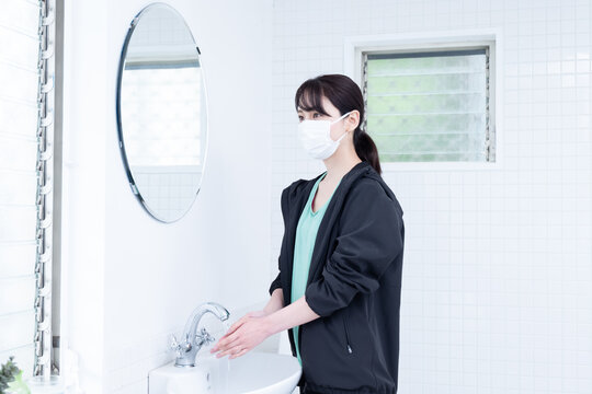 黒いジャージを着てマスクをして手を洗っている日本人女性