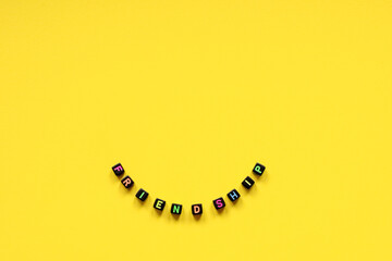 The word friendship composed from cubes with multicolored letters on a yellow background. A close-up. In the form of a smile.