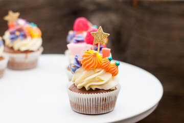Chocolate cupcakes with cream cheese frosting, chewing marmalade, sweets and golden topper on dark background