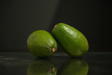 two whole avocados with reflection and copy space on a black background