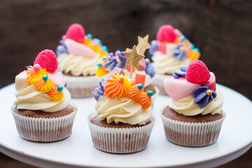 Chocolate cupcakes with cream cheese frosting, chewing marmalade, sweets and golden topper on dark background