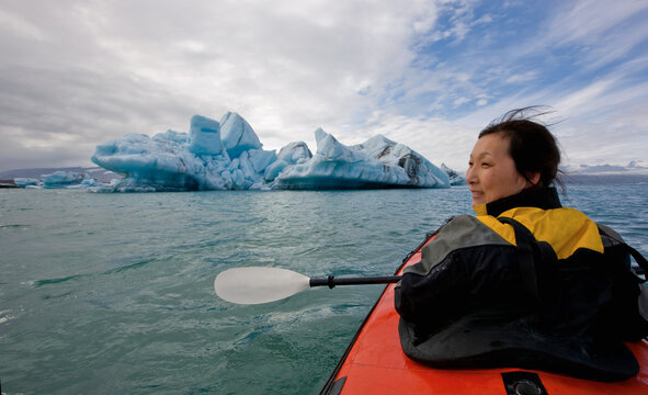 woman rowing sea kayak on J&circ;kuls&middot;rl&Ucirc;n glacier lagoon in Iceland