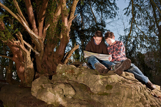 two boys reading map on top of rock