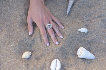 Hand with ring on the sand on a beach with seashells around