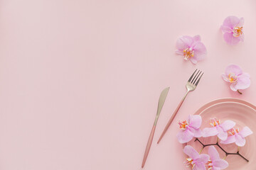 Flower and table settings overhead composition on light pink background. Pink ceramic plates, cutlery and perple orchid flowers. Holiday modern table decoration. Romantic date.