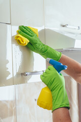 A woman wipes a yellow cloth kitchen cabinet, using a chemical from a bottle. Cleaning of the apartment. Light kitchen. kitchen cabinet