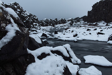 Amazing waterfall flowing down from volcanic black rocks covered by snow