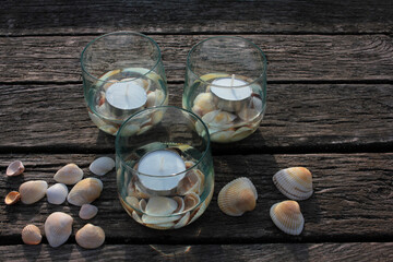 Tea candles in glasses and seashells on the beach wooden pier. Summer romantic evening 
