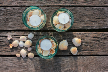 Tea candles in glasses and seashells on the beach wooden pier. Summer romantic evening 
